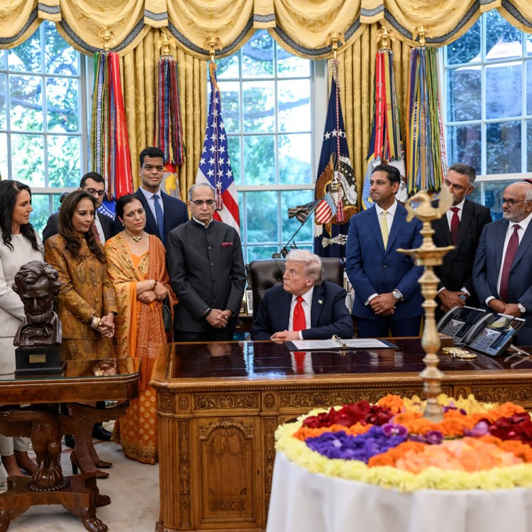 President Donald Trump participates in a Diwali celebration in the Oval Office with several attendees, including individuals in traditional attire and decorations including a floral arrangement.