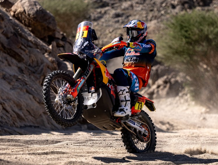 A motocross rider performing a wheelie on a dirt bike in a rugged terrain.