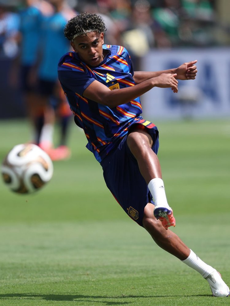 A football player in a blue and orange training kit executing a kick on the field during practice.