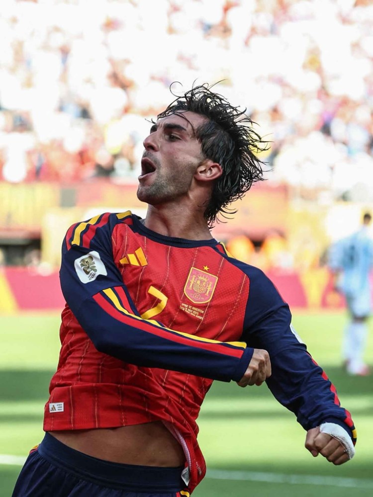 A soccer player in a red and blue Spanish national team jersey celebrating a goal with excitement.